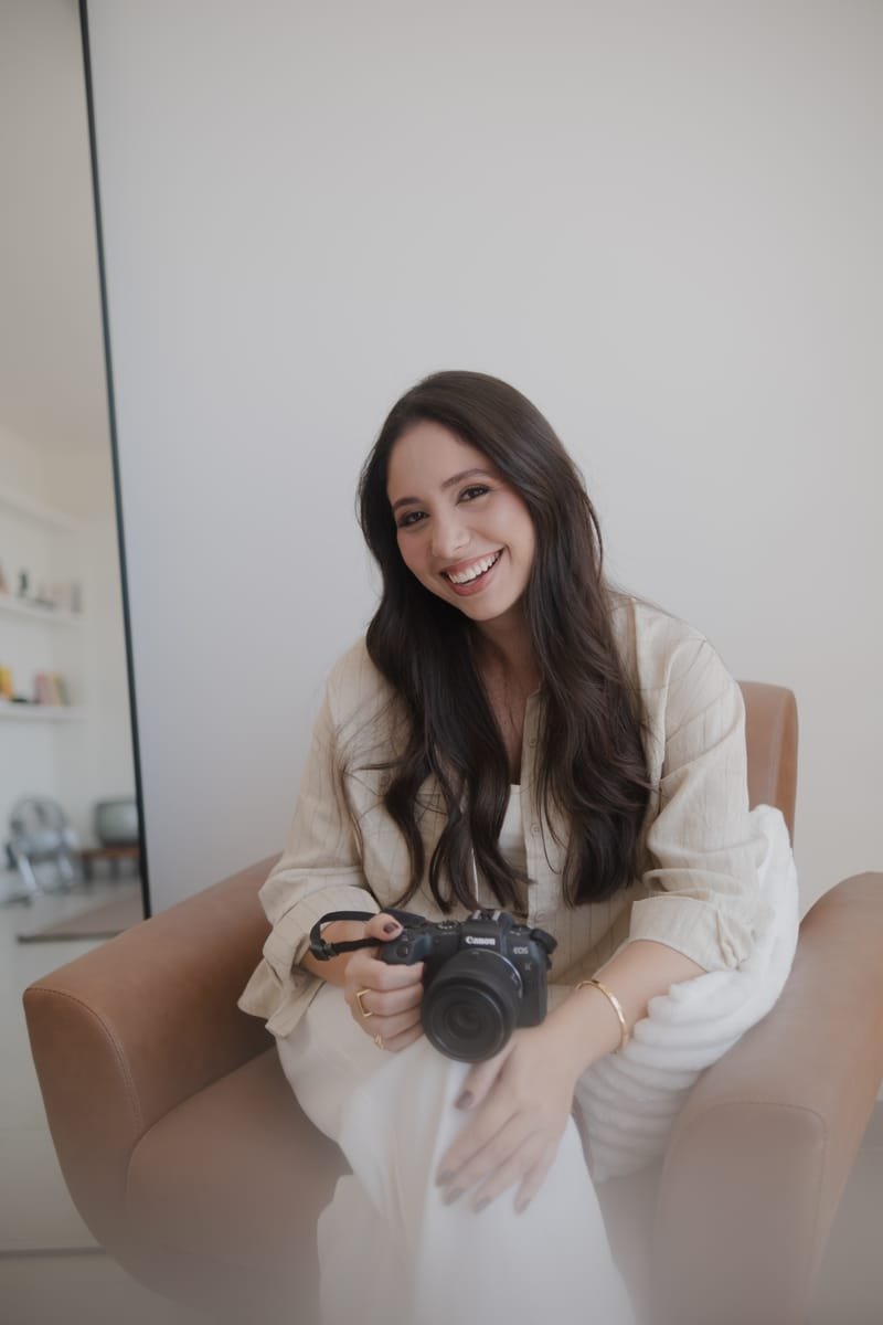 Bruna Gral sentada na poltrona com a camera no colo, sorrindo